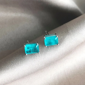 Macro shot of rectangular blue zircon earrings with four-claw silver setting on silk