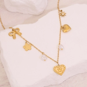 Golden multi-pendant necklace featuring bow, heart, and pearl charms on a white stone