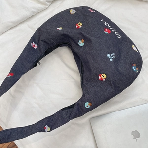 Detail of embroidered denim crescent bag with cartoon patches and white logo on blue fabric