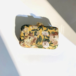 Macro shot of yellow silk evening clutch with floral embroidery and pearl clasp