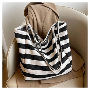 Detail of a large striped canvas tote bag with shoulder straps on a modern beige chair