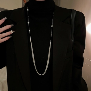 Detailed view of layered pearl necklace on a black turtleneck and tailored blazer