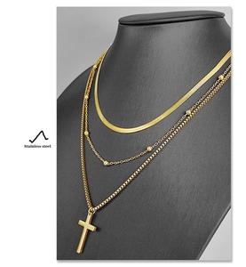 Detail of layered gold stainless steel necklace featuring snake chain and cross pendant