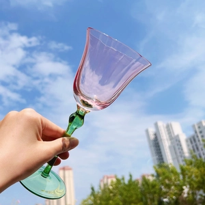 Pink flower-shaped wine glass with green stem held against a clear blue sky background
