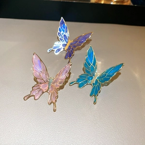 Three vintage enamel butterfly ear clips in pink, blue, and purple on a soft leather base