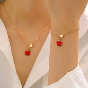 Dettaglio di un set di gioielli con mela smaltata rossa e cuore d'oro indossato da una modella