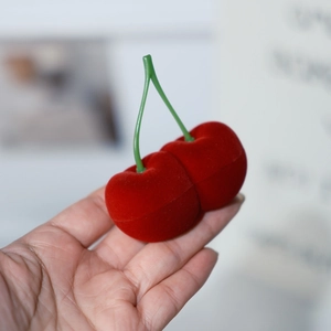 Primer plano de una mano sosteniendo un joyero de terciopelo con forma de cereza