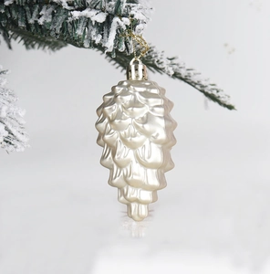 Creamy beige pine cone ornament with gold string hanging on a snowy Christmas branch