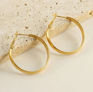 Macro shot of minimalist gold stainless steel hoop earrings resting on textured stone