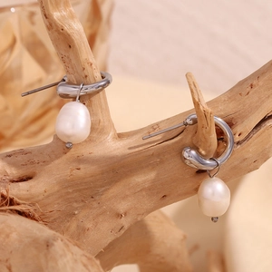 Silver hoop earrings with natural white freshwater pearl drops displayed on wood branch