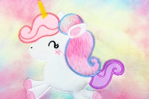 Macro detail of plush unicorn embroidery on colorful tie-dye fabric ipad sleeve