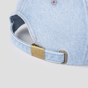 Close-up of adjustable brass buckle and denim texture on back of washed baseball cap