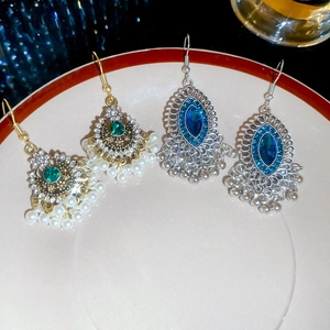 Dettaglio di orecchini vintage con diamanti e nappe di perle presentati su un piatto decorato