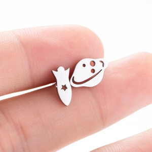 Minimalist stainless steel rocket and Saturn stud earrings shown on fingertip for scale
