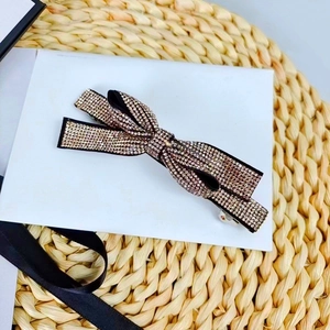 Close-up of black bow hair clip with champagne rhinestones on a woven background
