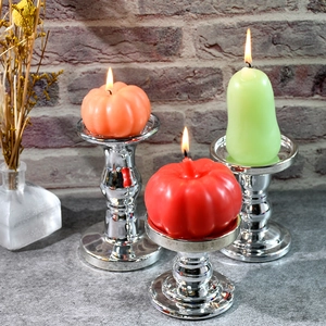 Tre eleganti portacandele in argento con candele a forma di zucca e pera su fondo mattoni
