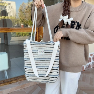 Close-up of a striped canvas tote bag with woven handles and a decorative brand patch