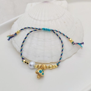 Bohemian woven rope bracelet with colorful beads and gold mushroom pendant on a seashell