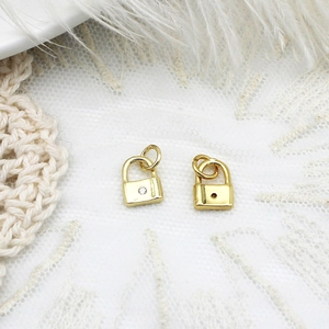 Detailed view of two gold mini padlock pendants with zircon inlay on white lace and feather