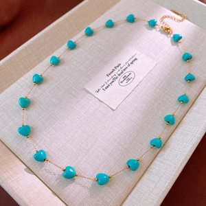 Detail showing a gold chain necklace with turquoise blue heart beads on a display tray