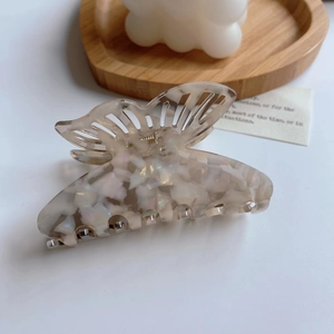Detailed close-up of a pearlescent butterfly hair claw clip on a clean aesthetic background