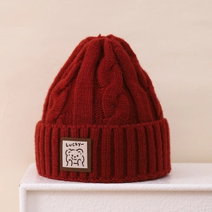 Detail of burgundy cable knit winter hat featuring a cute bear patch with Lucky text