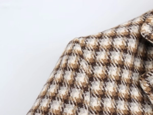 Detailaufnahme von braunem Tweed-Karo-Stoff mit feinen Goldfäden und präzisen Nähten am Kragen