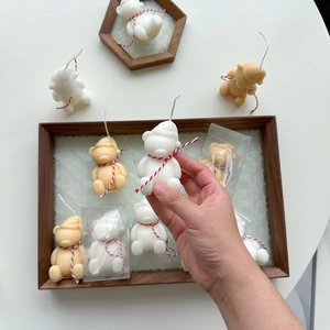 Close-up of hand holding mini teddy bear candles with festive woven rope on wood tray