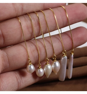 Close-up of gold box chain earrings with natural white baroque pearls held in hand