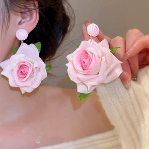 Close-up of pink fabric rose earrings with green leaves worn by a model in warm light