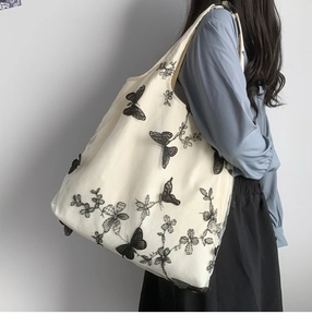 Vista laterale della borsa tote bianca con ricamo a farfalla in pizzo nero su modella