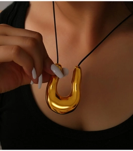Detailed view of a gold U-shaped geometric pendant on a minimalist black woven cord necklace