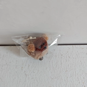 Detail of a brown plush puppy ornament with white hanging string in a package