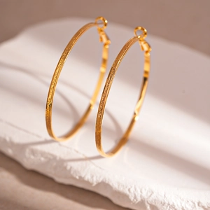 Detail of large gold hoop earrings with hammered metal texture on a stone base