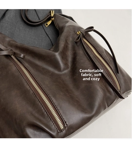 Detail of dark brown leather tote featuring side zipper with decorative bow ribbon knot