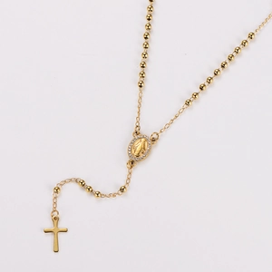 Detailed view of golden rosary necklace with cross and Virgin Mary charms on white backdrop