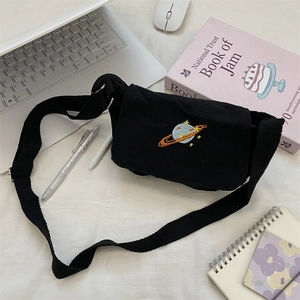 Flat lay of black canvas crossbody bag with planet embroidery on white desk setup