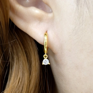 Macro shot of gold earring with round clear stone on model ear for elegant look