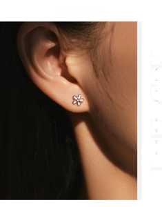 Close-up of a pink flower stud earring with a center stone on a model ear