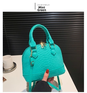 Detail of mint green shell bag featuring embossed crocodile pattern and gold zippers