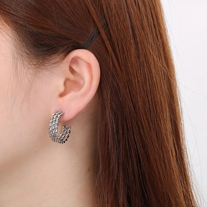 Close-up of silver-tone twisted rope hoop earrings worn on ear showing detailed metal texture