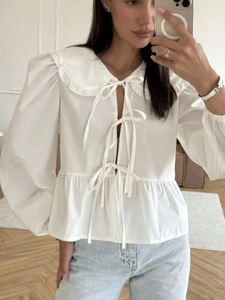 Detail of white cotton blouse featuring ruffle collar and triple bow tie closures