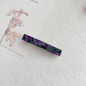 Detail of elegant marbled acetate hair clip with purple and green textures on floral card