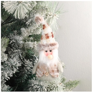Close-up of a plush Christmas gnome with beige plaid hat hanging on a snowy tree branch