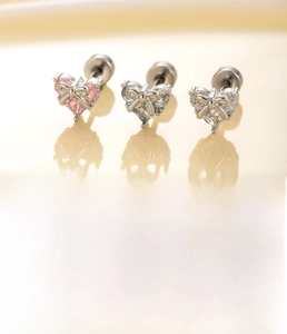 Détail macro de boucles d'oreilles cœur argentées avec nœud et zircons roses et bleus