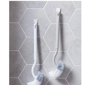 Detail view of the curved long handle toilet brush with wall-mounted hook on grey tiles
