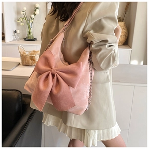 Detailed view of pink suede-like shoulder bag featuring a large bow and metal chain strap