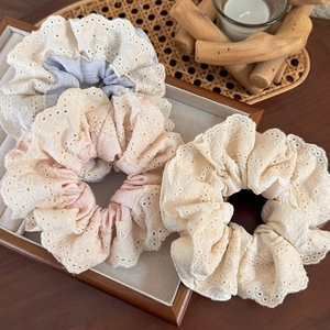 Detailed view of three floral lace scrunchies in beige, pink, and blue-grey colors