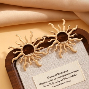 Close-up of golden sunburst earrings on a wooden display stand with silk background