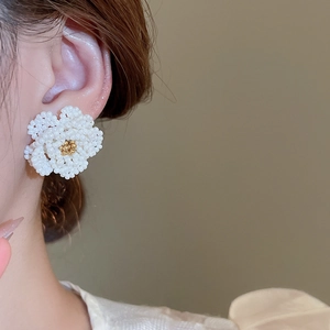 Close-up of camellia beaded earrings in pearl white woven design worn by model